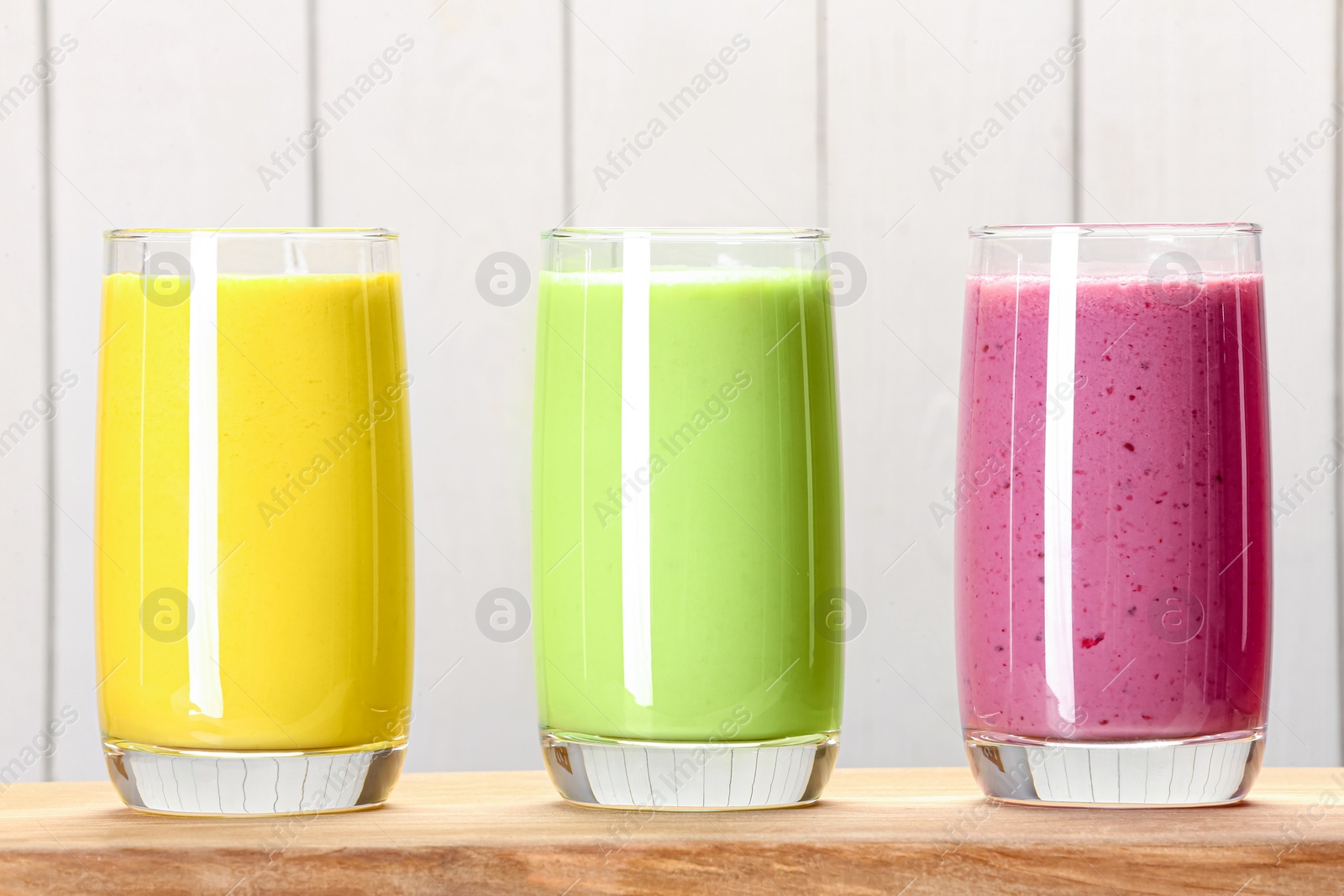 Photo of Board with many different tasty smoothies against white wooden background, closeup