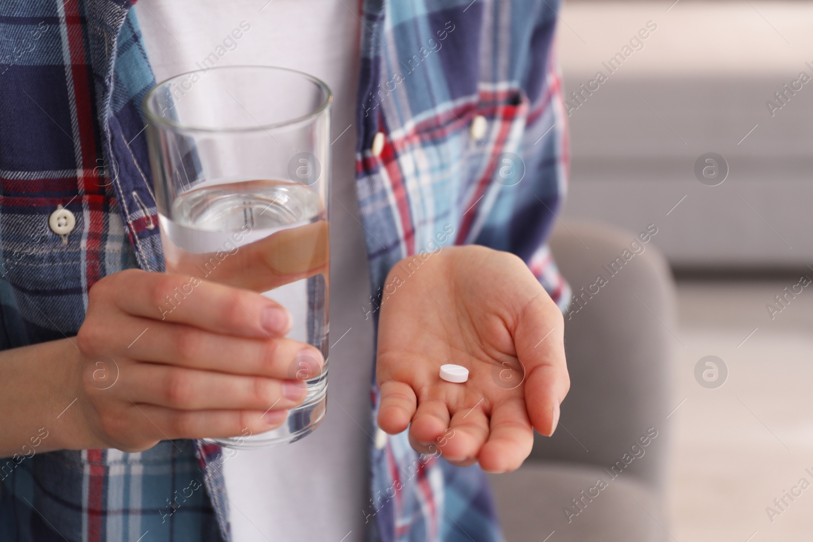 Photo of Young woman with abortion pill and glass of water indoors, closeup