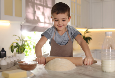Photo of Cute little boy rolling dough at table in kitchen. Cooking pastry