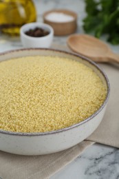 Photo of Bowl of raw couscous on white marble table, closeup