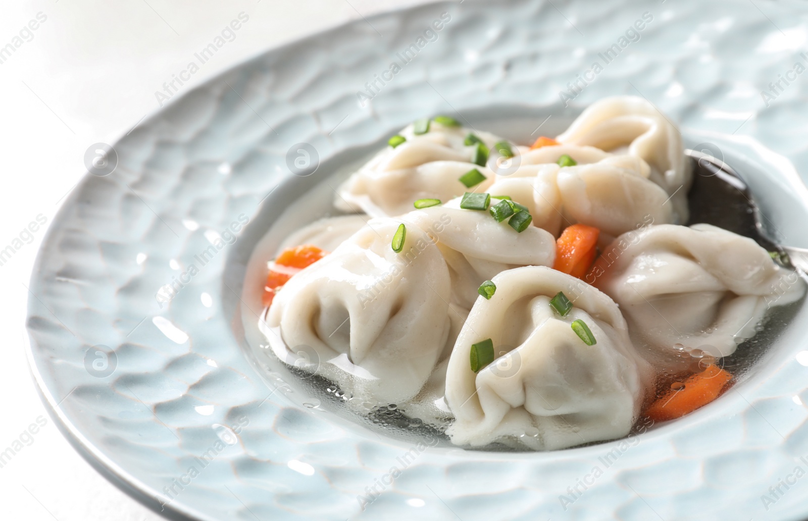 Photo of Plate of tasty dumplings in broth on light background, closeup