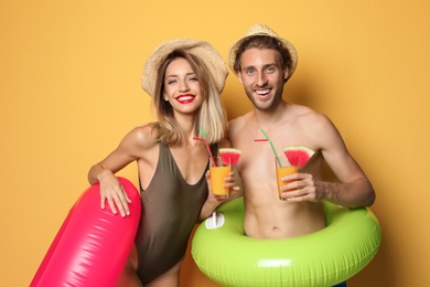 Photo of Happy young couple in beachwear with inflatable rings and cocktails on color background