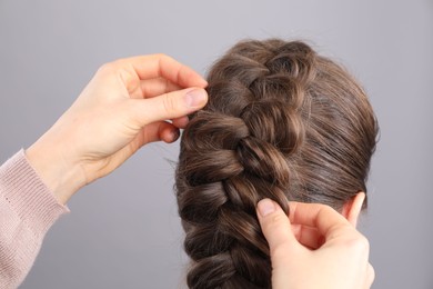 Photo of Professional stylist braiding woman's hair on grey background, closeup