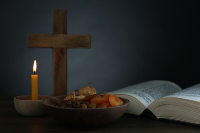 Photo of Cross, Bible, candle and dried fruits on wooden table, space for text. Lent season