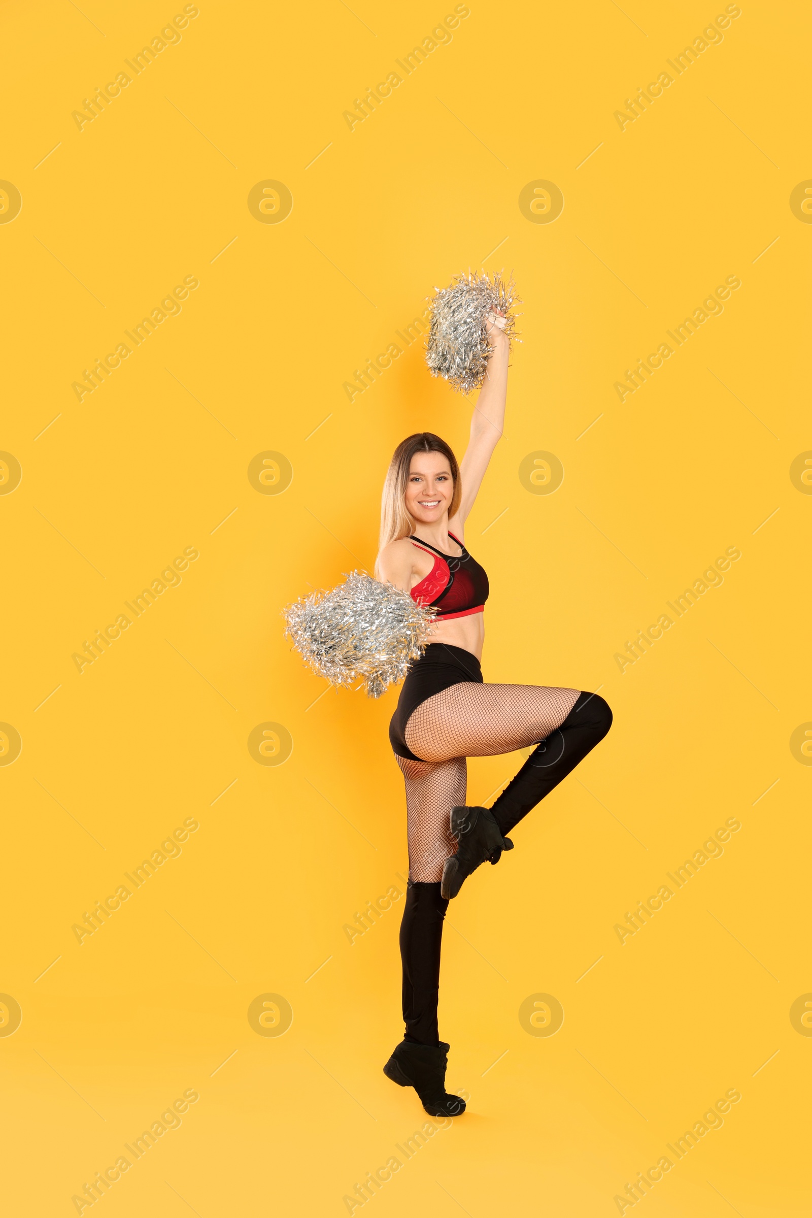 Photo of Beautiful cheerleader in costume holding pom poms on yellow background