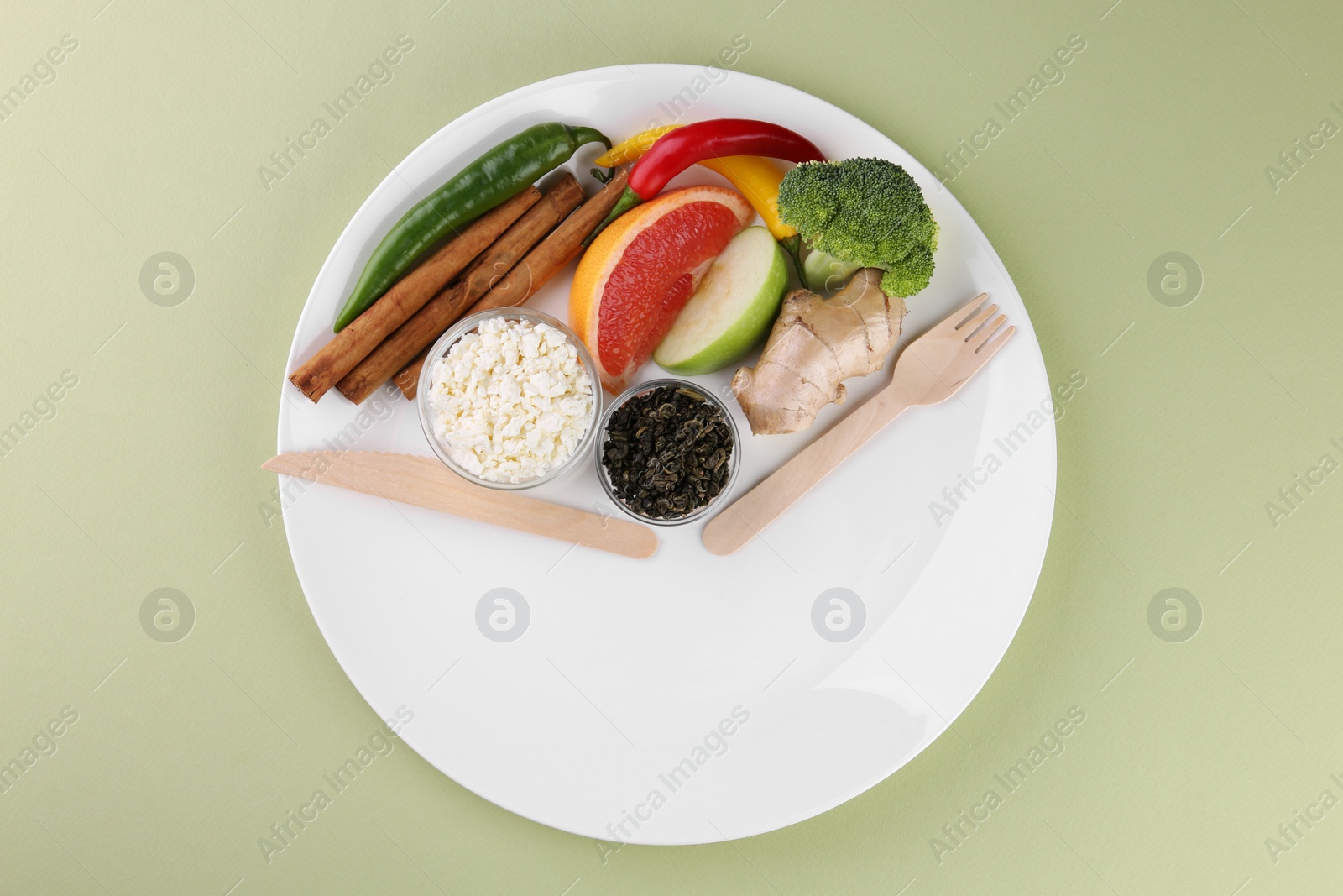 Photo of Metabolism. Plate with different food products and wooden cutlery on pale green background, top view