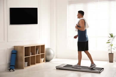 Photo of Sporty man training on walking treadmill while watching TV at home