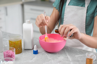 Photo of Little girl mixing ingredients with silicone spatula at table indoors, closeup. DIY slime toy