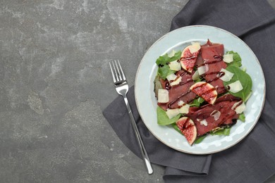 Photo of Plate with delicious bresaola salad served on grey textured table, flat lay. Space for text