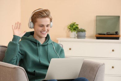 Photo of Teenage boy with headphones using laptop for video chat at home
