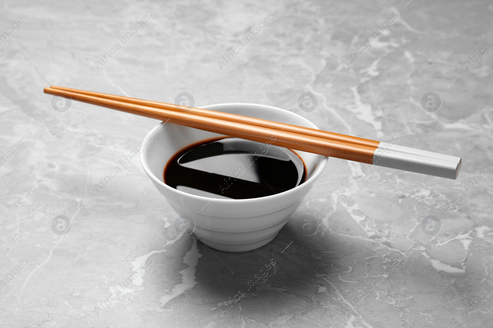 Photo of Bowl of soy sauce with chopsticks on marble background