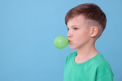 Photo of Boy blowing bubble gum on light blue background, space for text