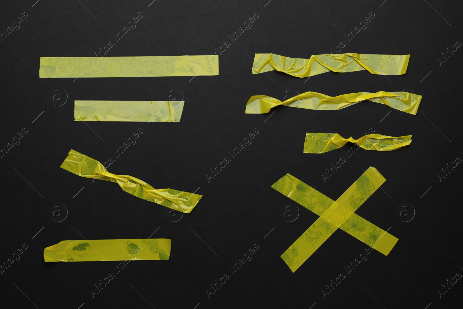 Photo of Many pieces of yellow adhesive tape on black background, flat lay