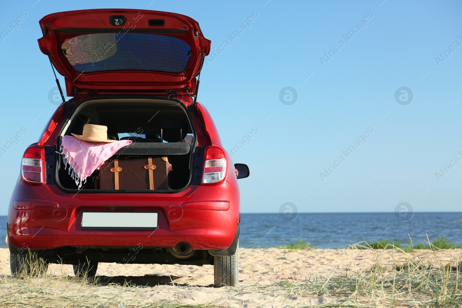 Photo of Retro suitcase and beach accessories in car trunk on sand near sea. Space for text