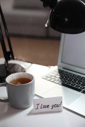 Photo of Note with handwritten text I Love You on workplace indoors. Romantic message