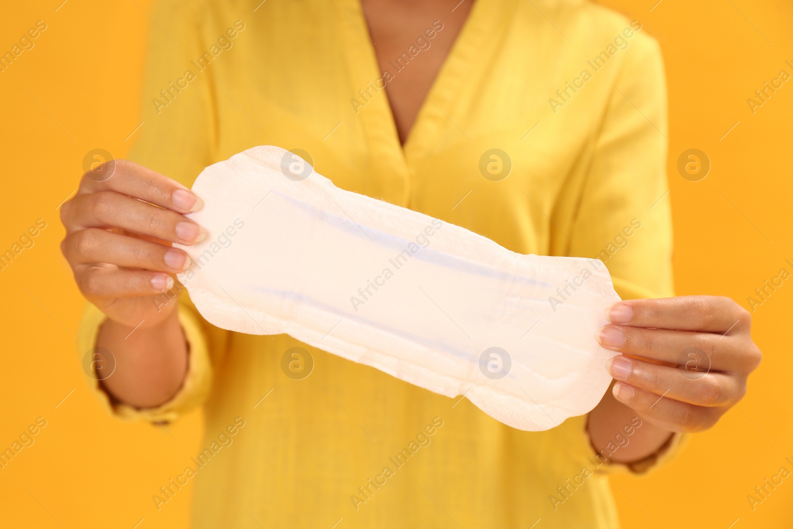 Photo of Young woman with menstrual pad on yellow background, closeup