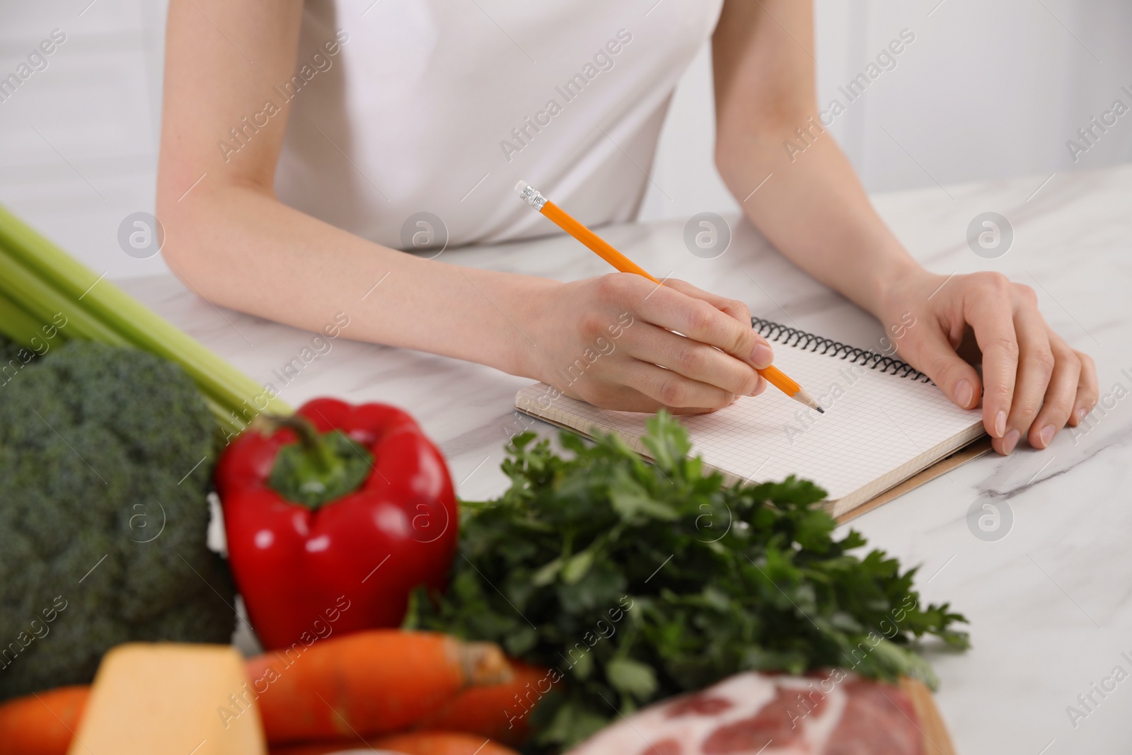 Photo of Woman with notebook and healthy food at white table, closeup. Keto diet