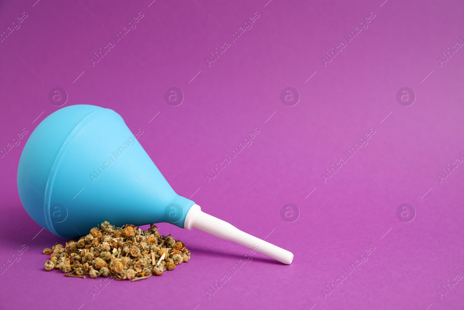 Photo of Blue enema and dry chamomile flowers on purple background. Space for text