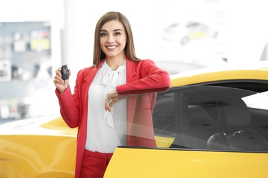 Photo of Young woman holding key near new car in salon