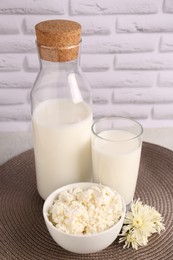 Photo of Tasty fresh milk and cottage cheese on mat against white brick wall