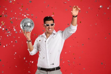 Photo of Happy man with disco ball and confetti on red background