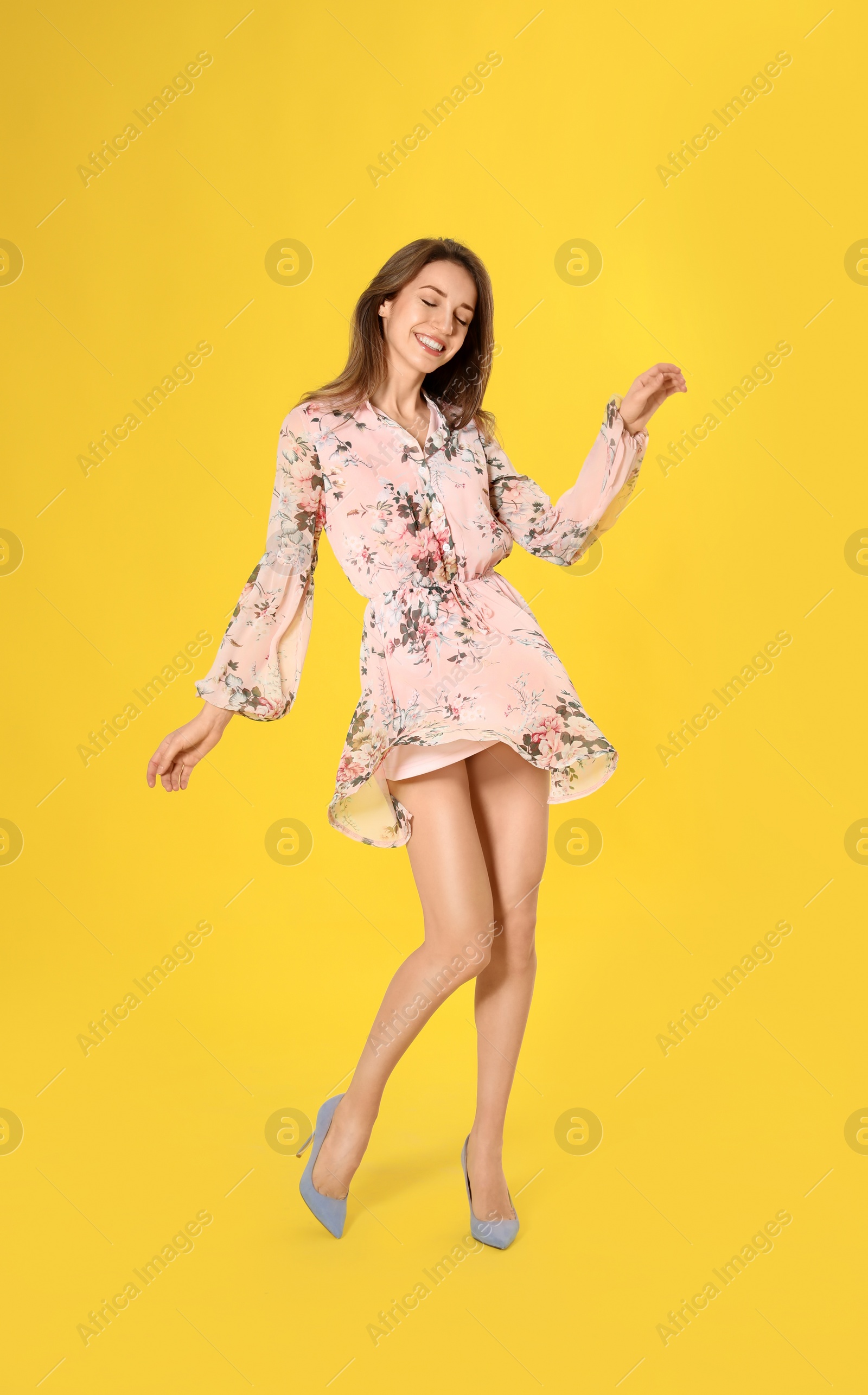 Photo of Young woman wearing floral print dress and elegant shoes on yellow background