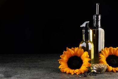 Photo of Sunflower cooking oil, seeds and beautiful flowers on grey table against black background. Space for text