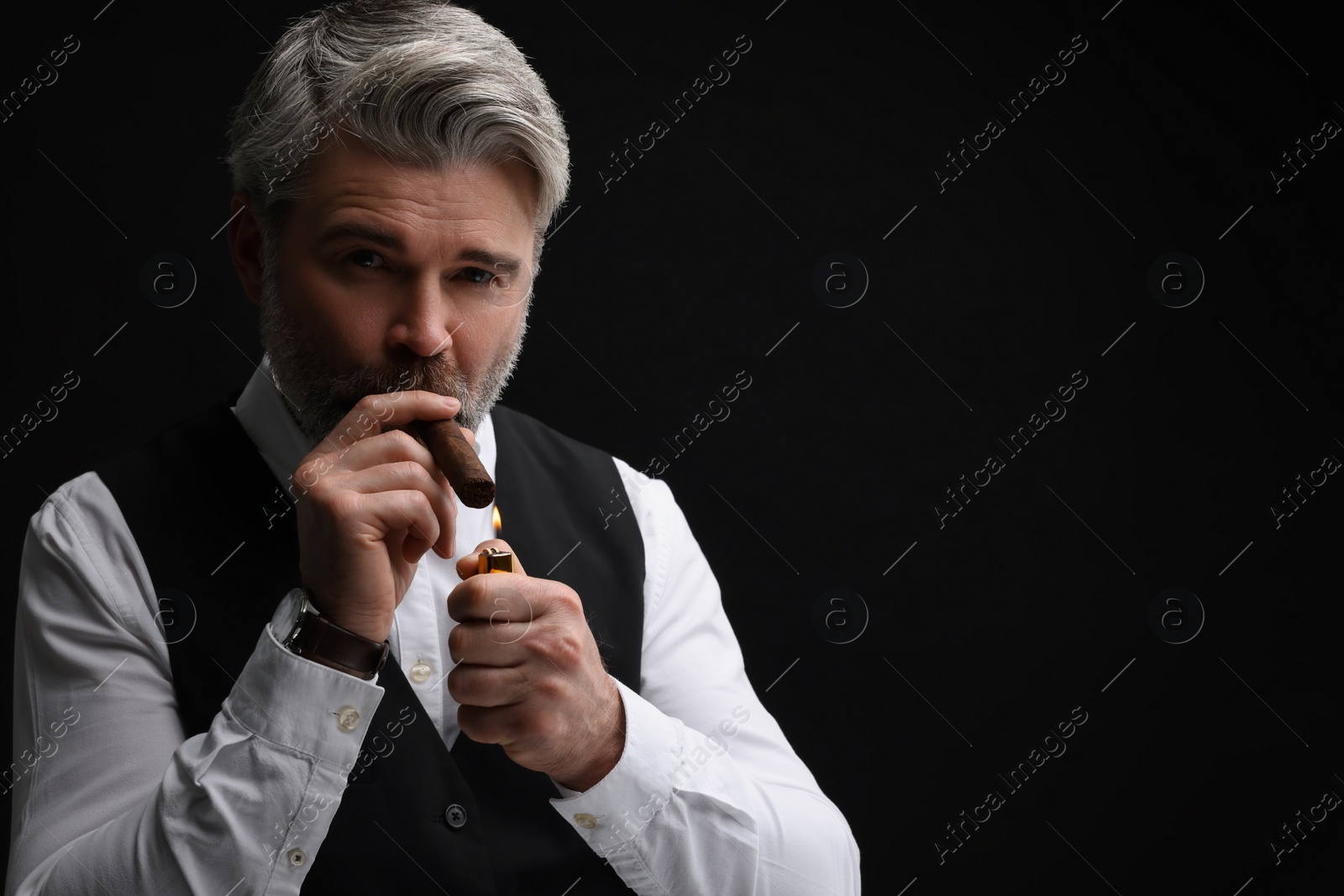 Photo of Bearded man lighting cigar on black background. Space for text