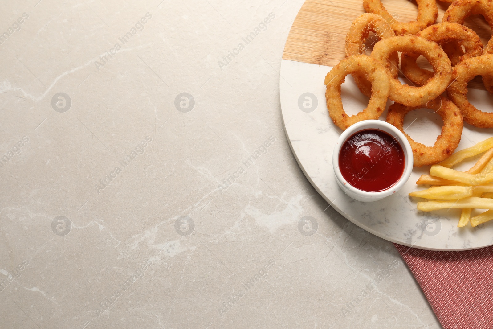 Photo of Board with tasty ketchup, fries and onion rings on marble table, top view. Space for text