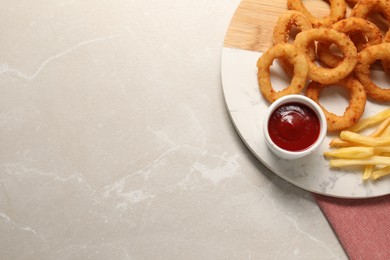 Board with tasty ketchup, fries and onion rings on marble table, top view. Space for text