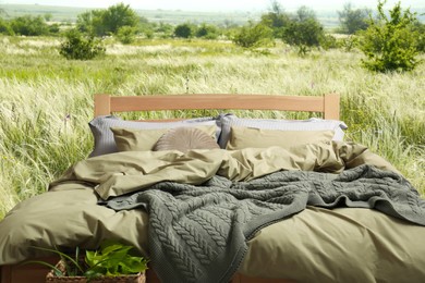 Image of Comfortable bed with soft pillows in meadow on sunny day