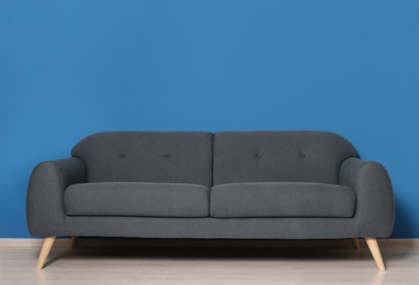 Photo of Stylish grey sofa near blue wall in room. Interior design