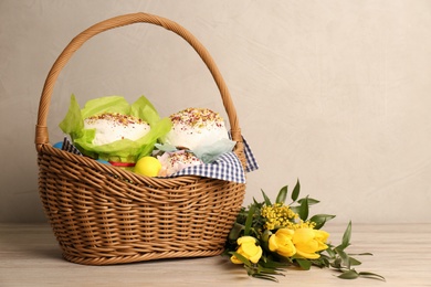 Photo of Basket with delicious Easter cakes, dyed eggs and flowers on wooden table