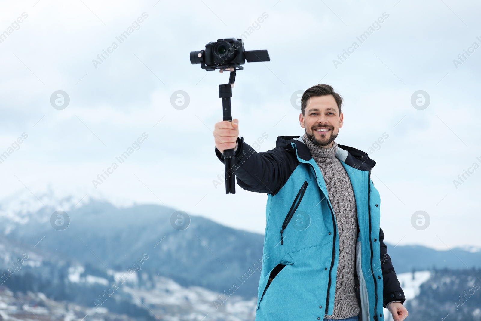 Photo of Man with stabilizer and camera recording video in mountains. Winter vacation