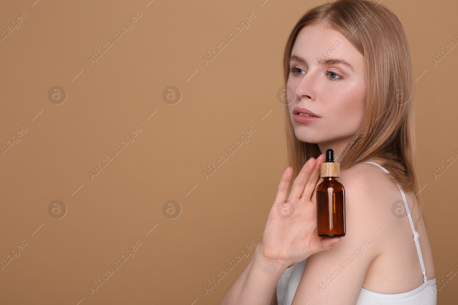 Photo of Beautiful young woman with essential oil on brown background. Space for text