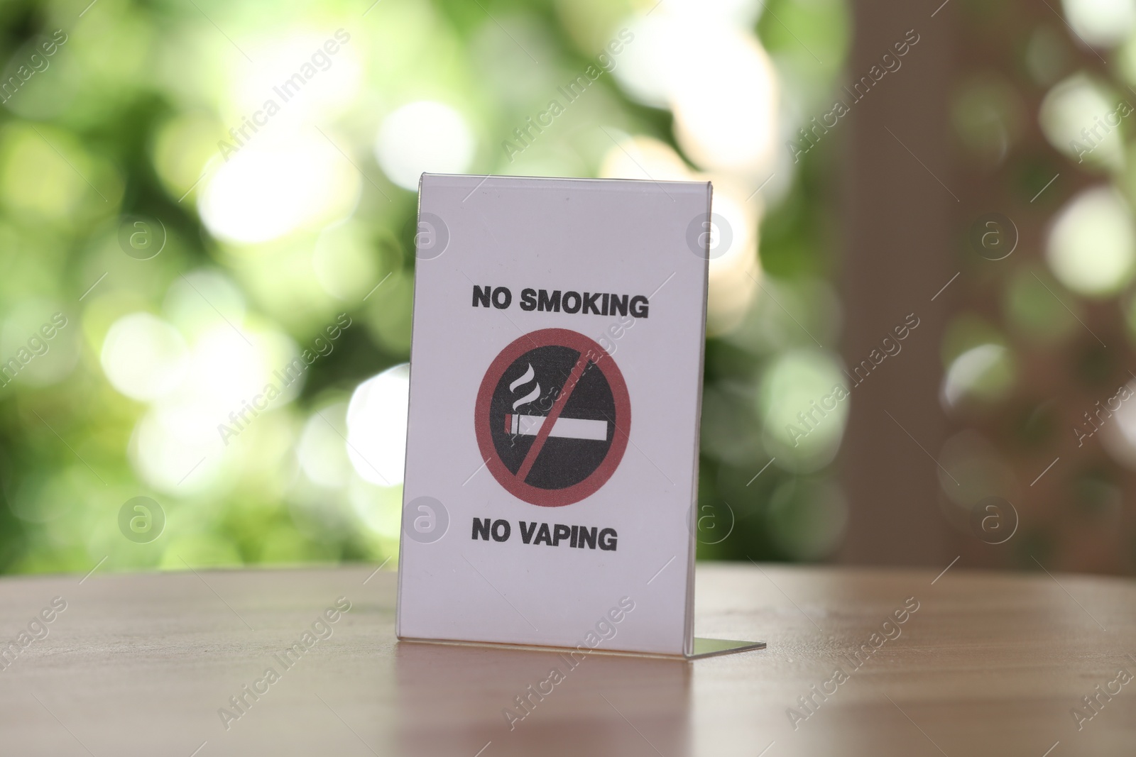 Photo of No Smoking No Vaping sign on wooden table against blurred background