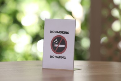 No Smoking No Vaping sign on wooden table against blurred background