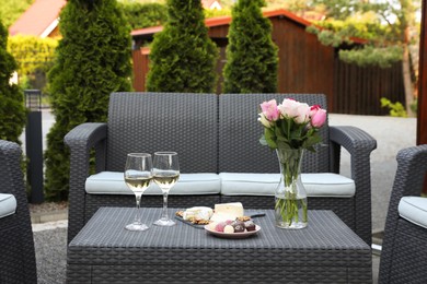 Vase with roses, glasses of wine and food on rattan table on outdoor terrace