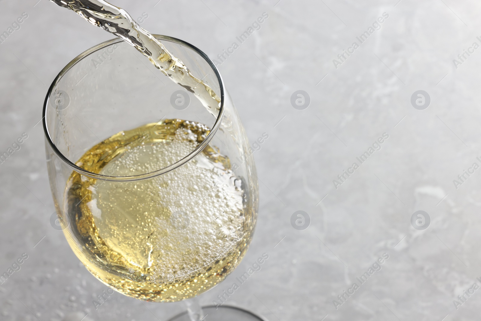 Photo of Pouring tasty aromatic wine in glass at gray marble table, closeup. Space for text