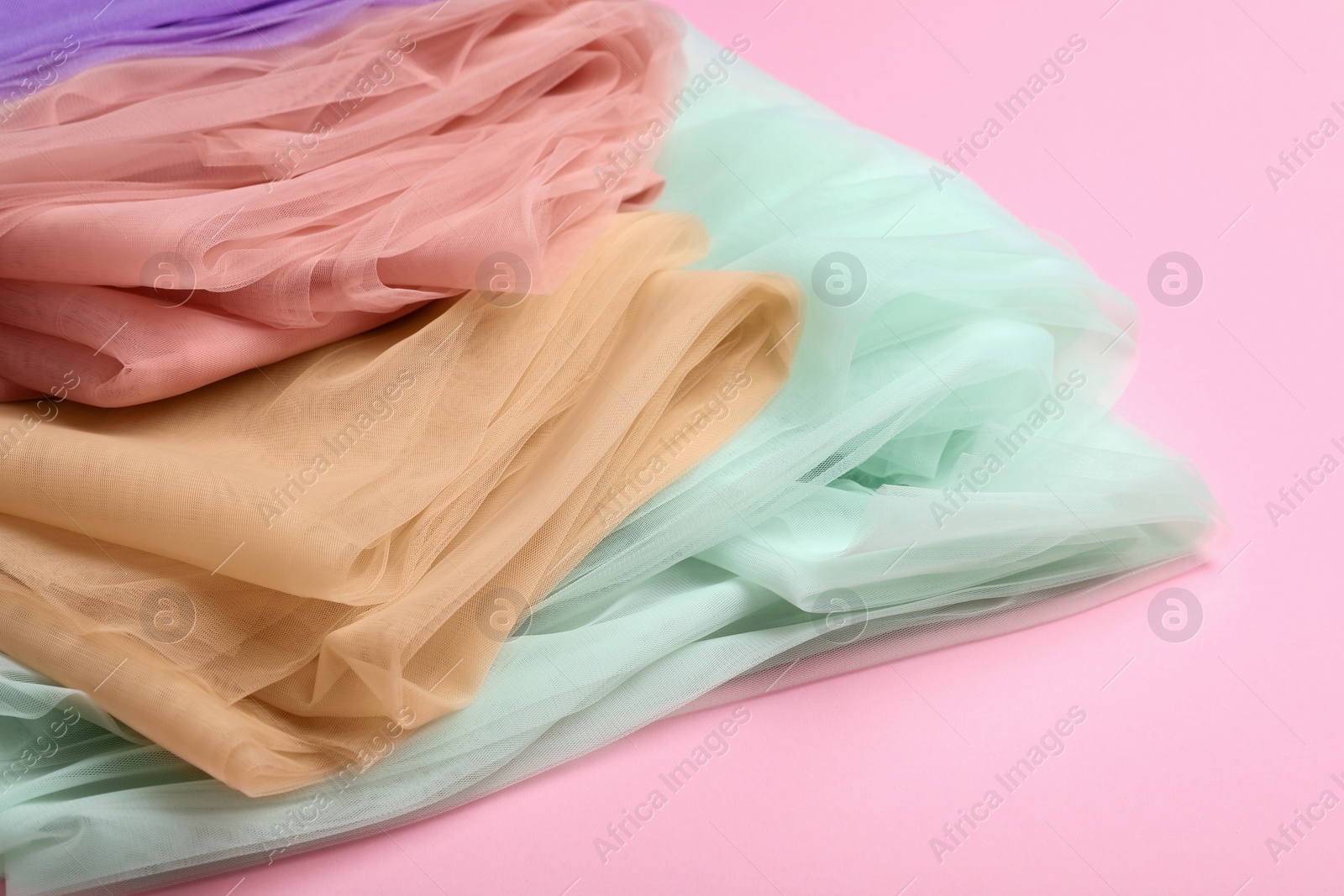 Photo of Beautiful colorful tulle fabrics on pink background, closeup