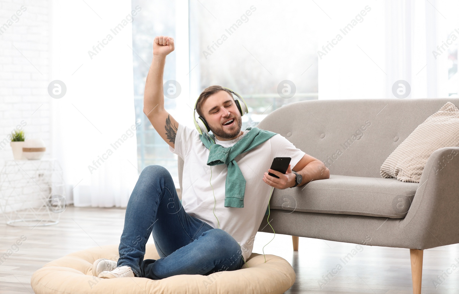 Photo of Young man with headphones and mobile device enjoying music on floor in living room