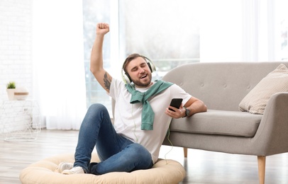 Young man with headphones and mobile device enjoying music on floor in living room