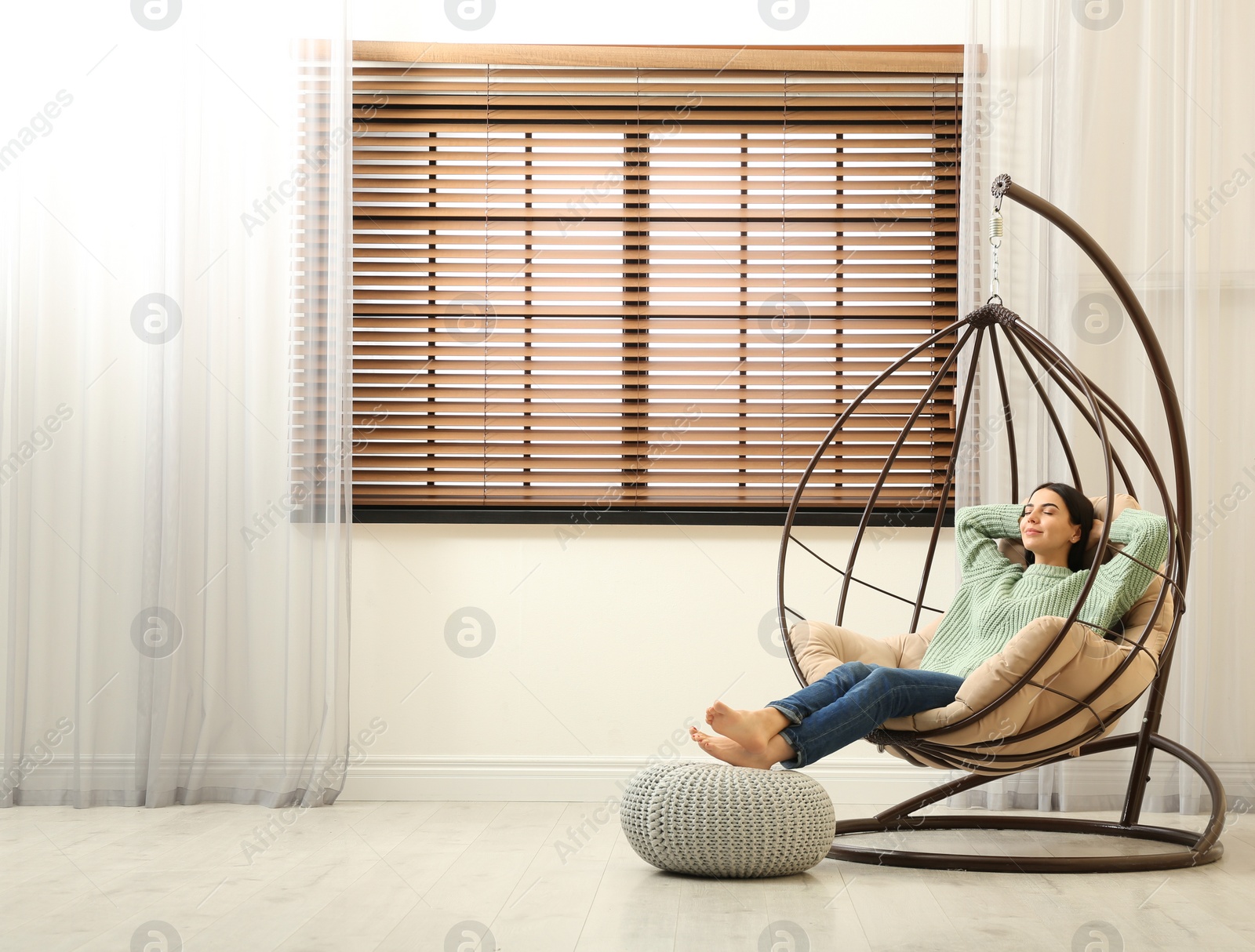 Photo of Young woman relaxing in hanging chair near window at home. Space for text