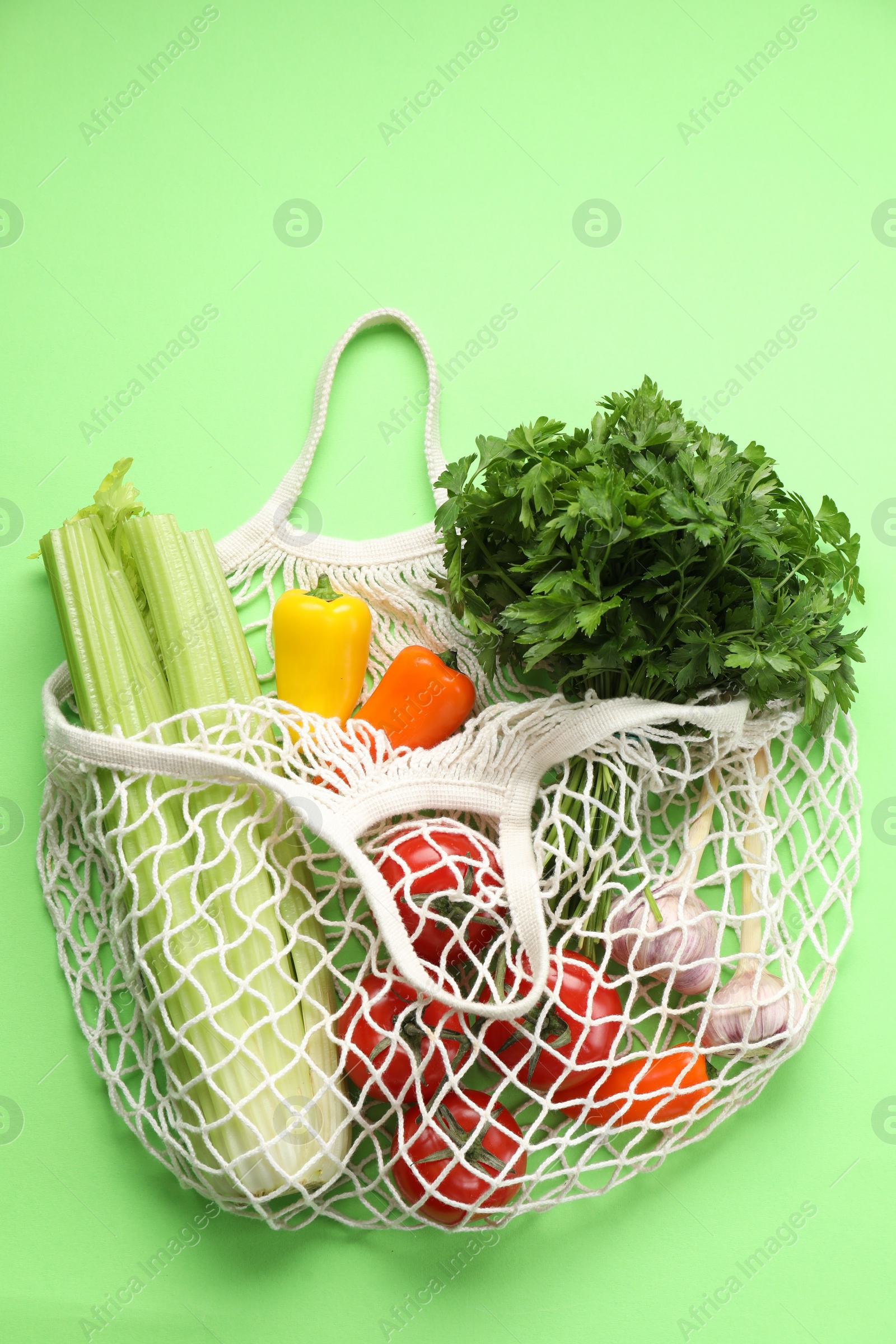 Photo of String bag with different vegetables on light green background, top view
