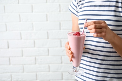 Photo of Woman holding glass of tasty smoothie with raspberries and straw against white brick wall, closeup. Space for text