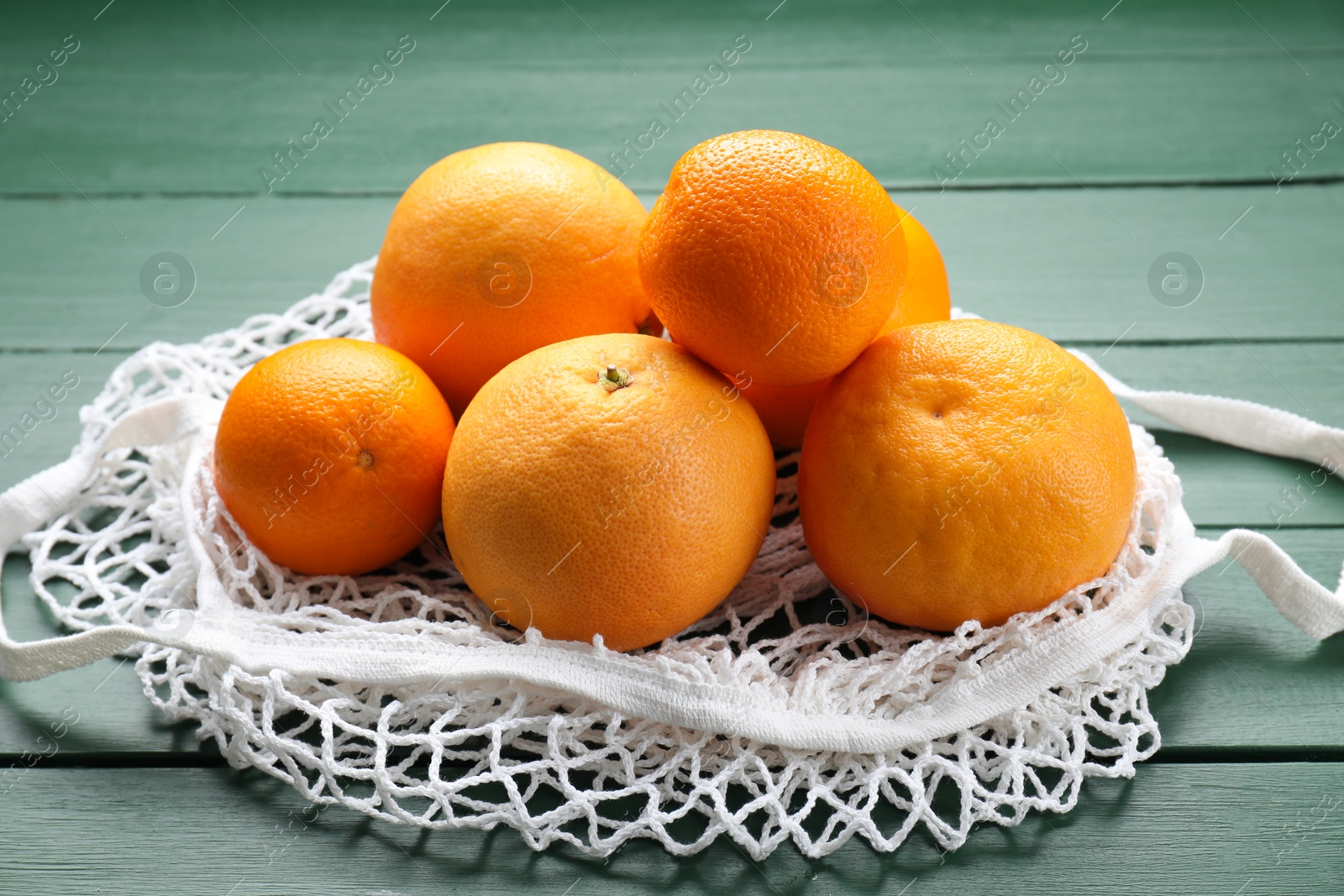 Photo of String bag with oranges on green wooden table, closeup