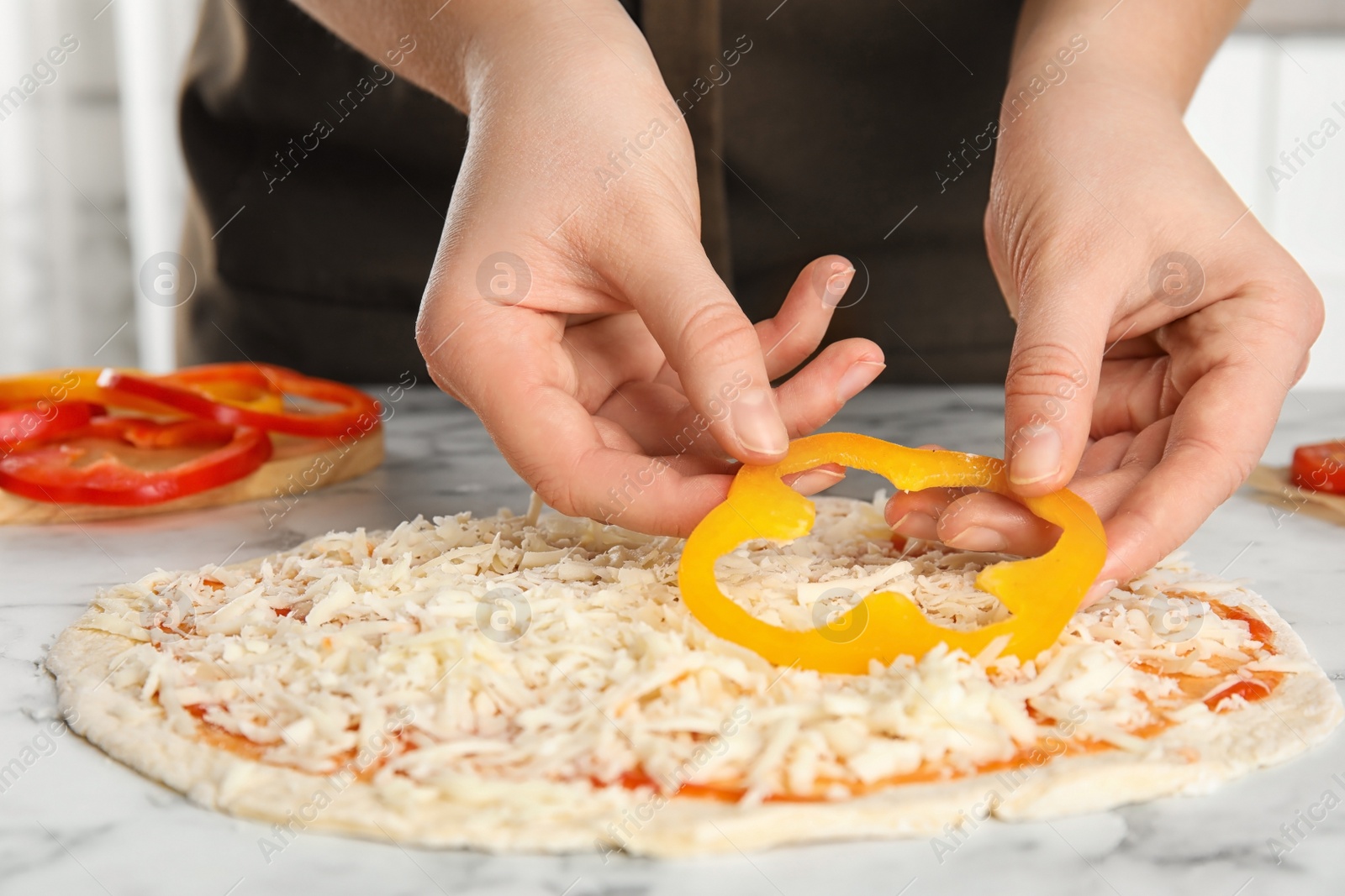 Photo of Woman adding bell pepper to pizza white marble table, closeup