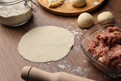 Photo of Dough, minced meat, flour and rolling pin on wooden table. Making chebureki