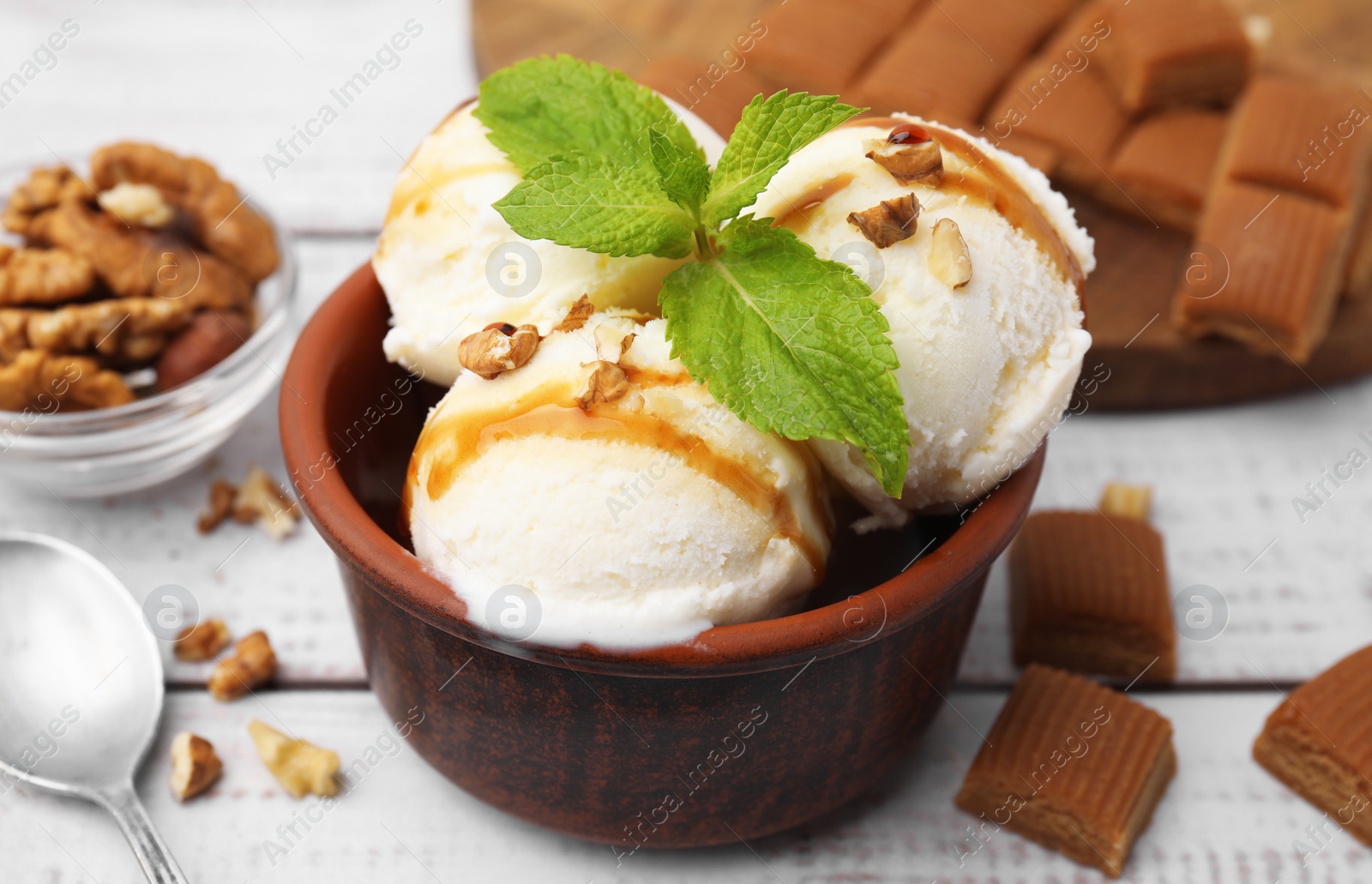 Photo of Bowl of tasty ice cream with caramel sauce, mint and nuts on white wooden table, closeup