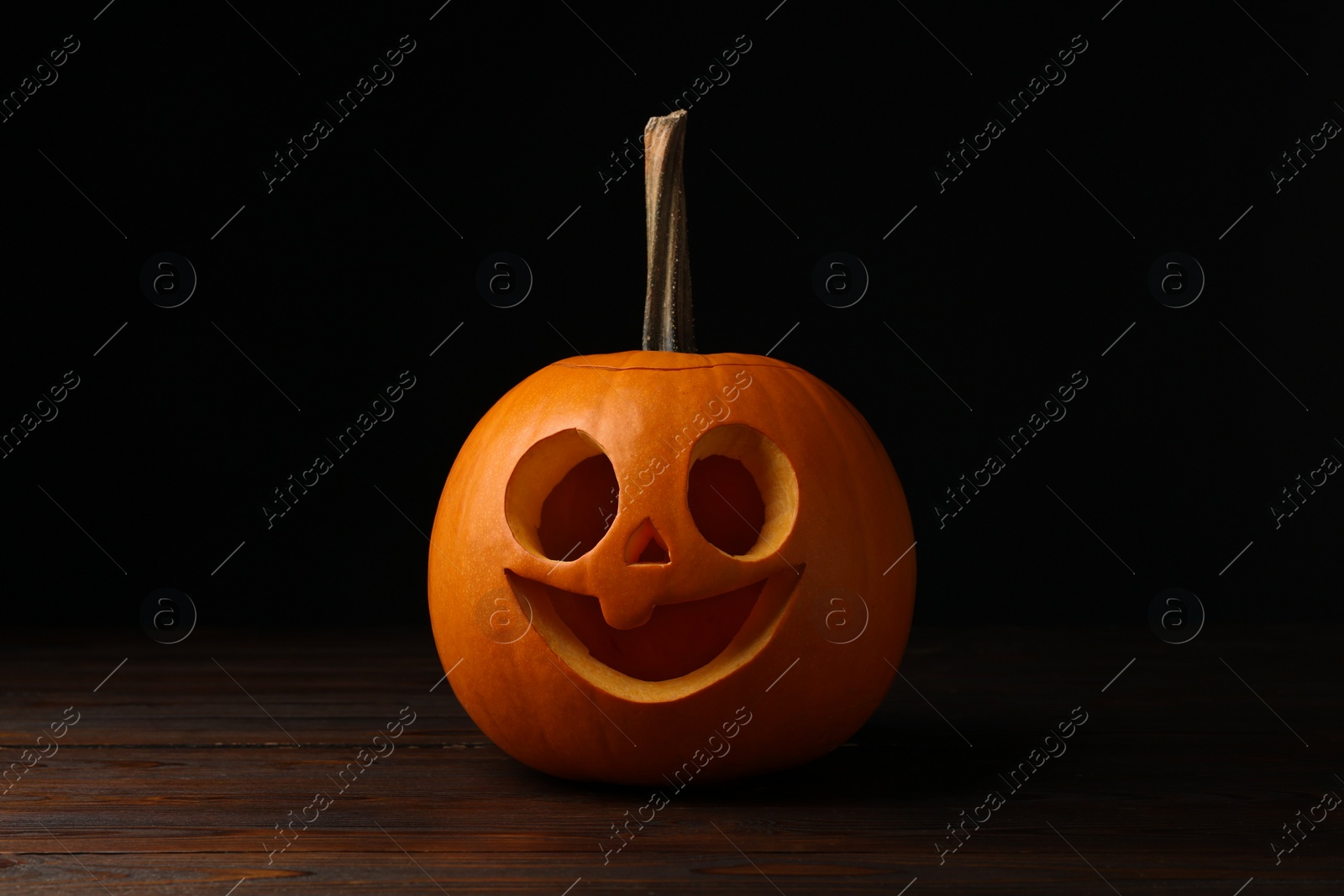 Photo of Scary jack o'lantern made of pumpkin on wooden table in darkness. Halloween traditional decor